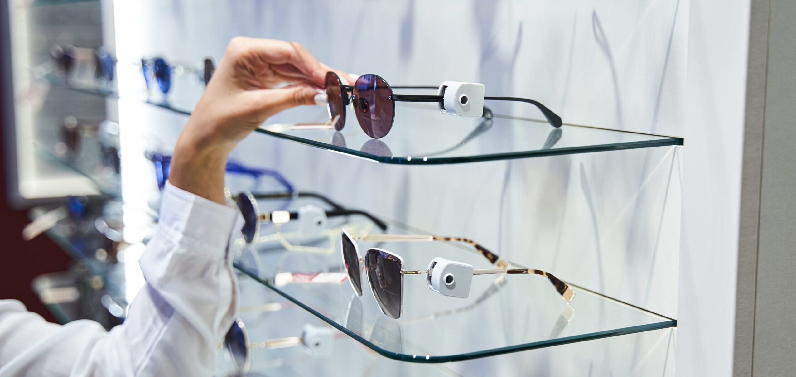 Close up of young woman standing by glass showcase and choosing shades in eyeglasses store